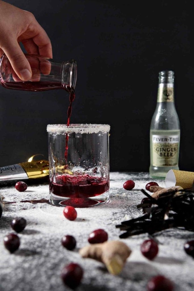 Cranberry juice is poured into a glass to make a Sparkling Ginger Cranberry Mocktail