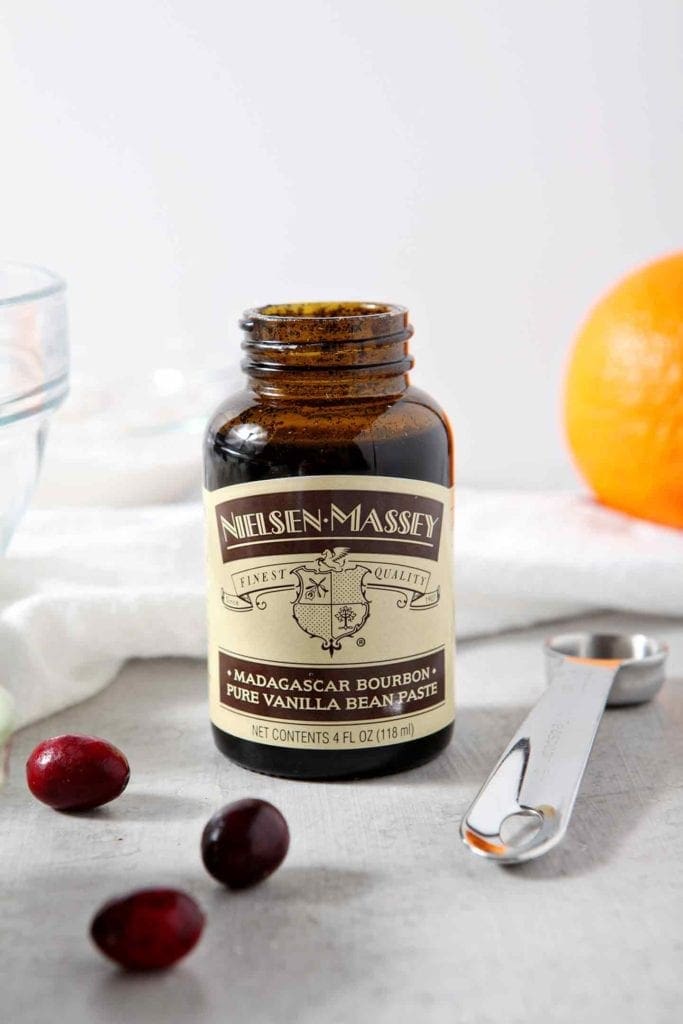 A bottle of Vanilla Bean Paste sits on a grey tabletop with a measuring spoon