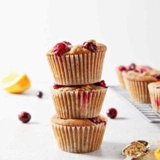 A stack of three Vegan Orange Cranberry Muffins stand beside a wire cooling rack with more muffins