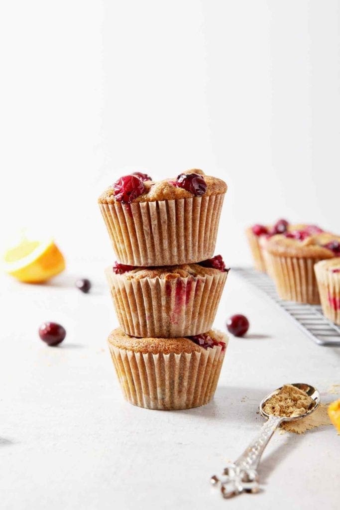 A stack of three Vegan Orange Cranberry Muffins stand beside a wire cooling rack with more muffins