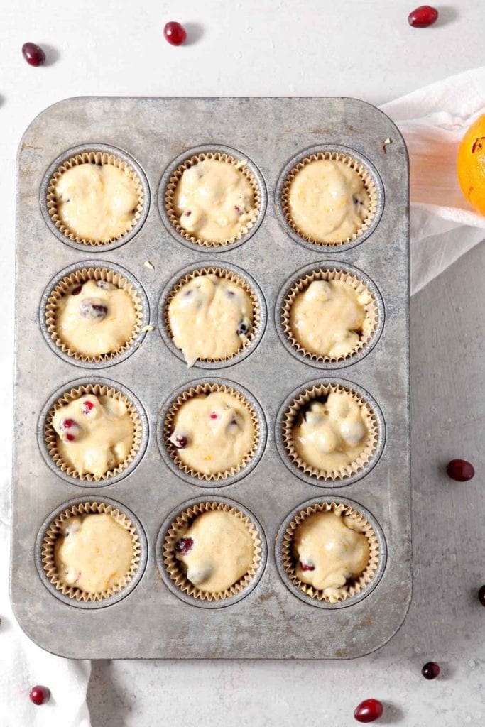 Vegan Orange Cranberry Muffins are scooped into muffin tins, before baking