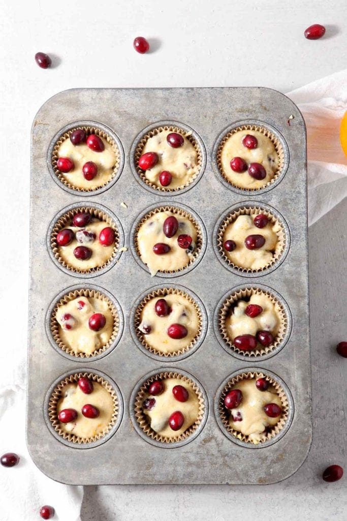 Vegan Orange Cranberry Muffins are scooped into muffin tins, before baking