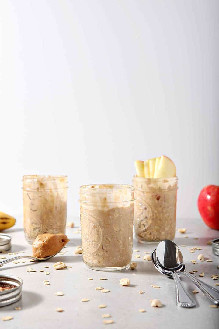 Three jars of Peanut Butter Overnight Oats are shown on a grey background with various toppings