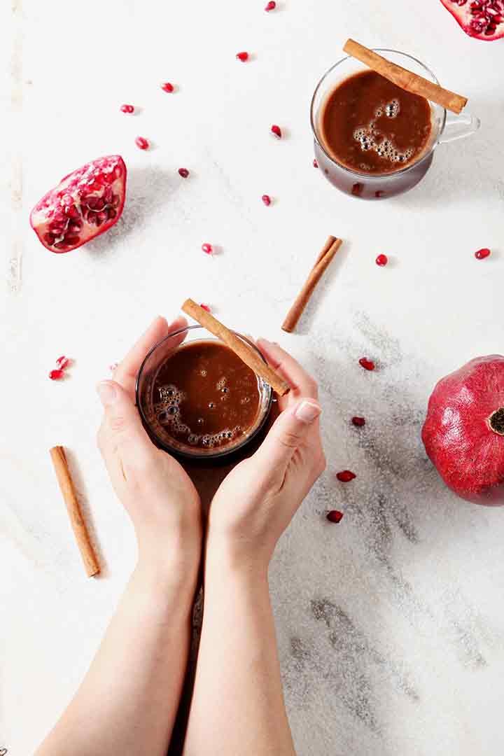 A woman holds a mug of Pomegranate Hot Buttered Rum with both hands