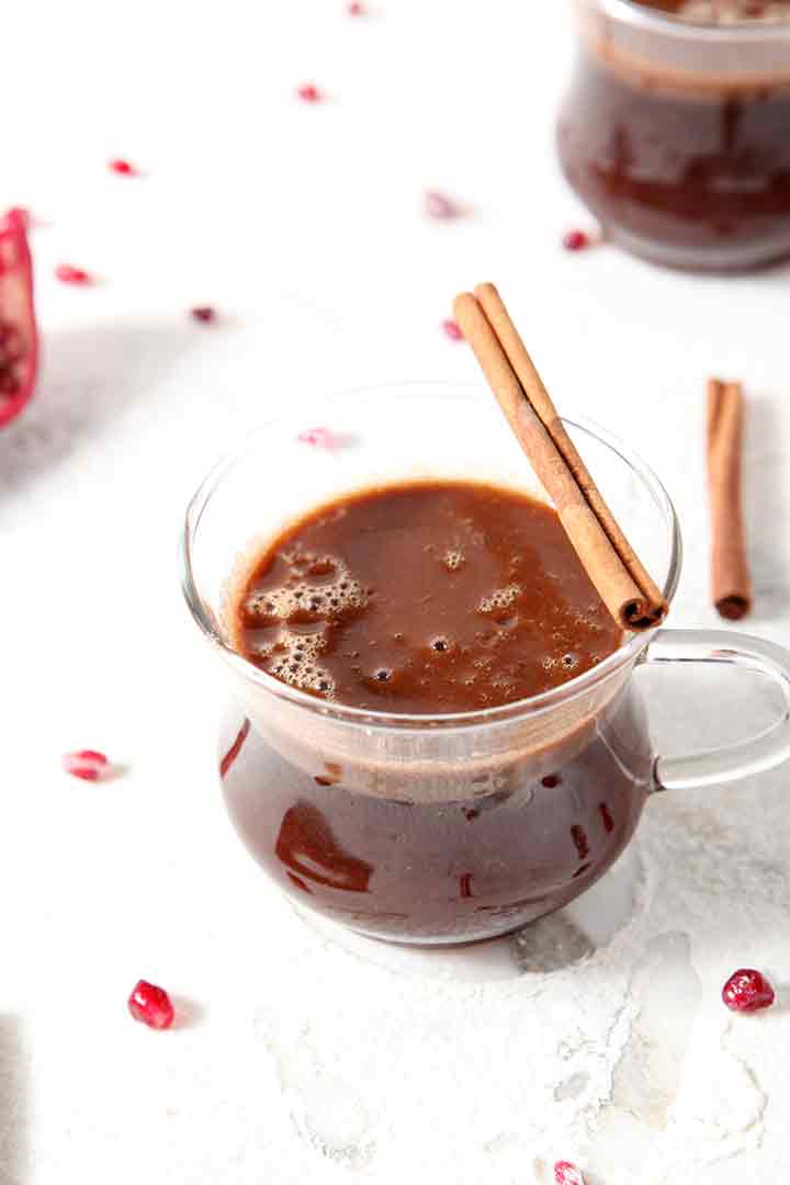 A close up of a glass mug holding Pomegranate Hot Buttered Rum, garnished with a cinnamon stick