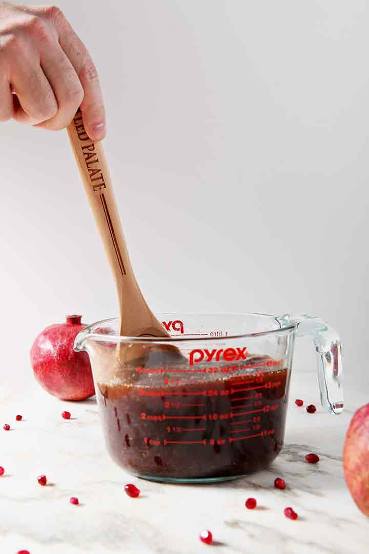 A man stirs Pomegranate Hot Buttered Rum in a glass measuring cup with a wooden spoon