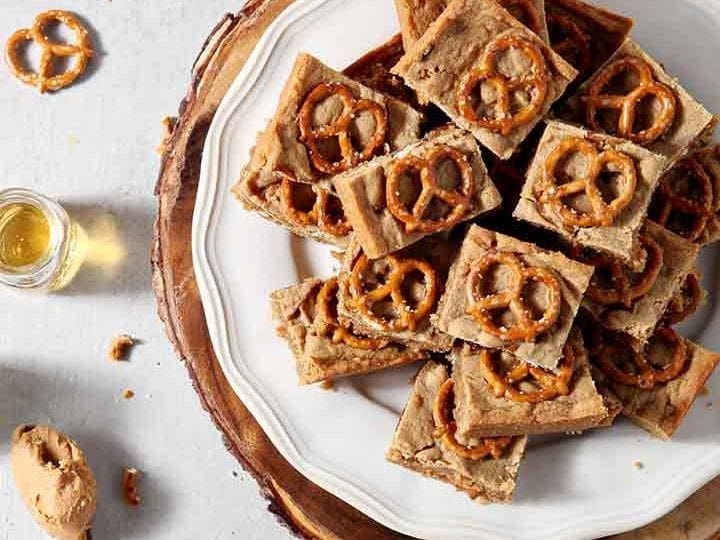 Boozy Bacon Pretzel Peanut Butter Bars are served on a round white plate