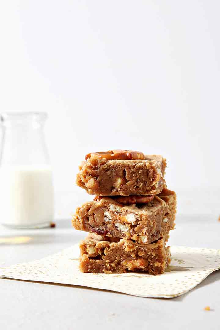 Three Boozy Bacon Pretzel Peanut Butter Bars are stacked on top of each other in front of a bottle of milk