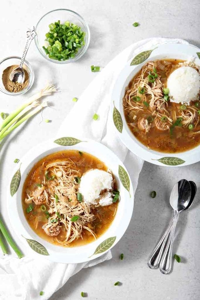 Two bowls of Chicken and Sausage Gumbo are served with rice and green onions