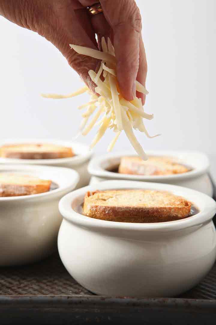 A woman sprinkles cheese on top of the French Onion Soup crocks