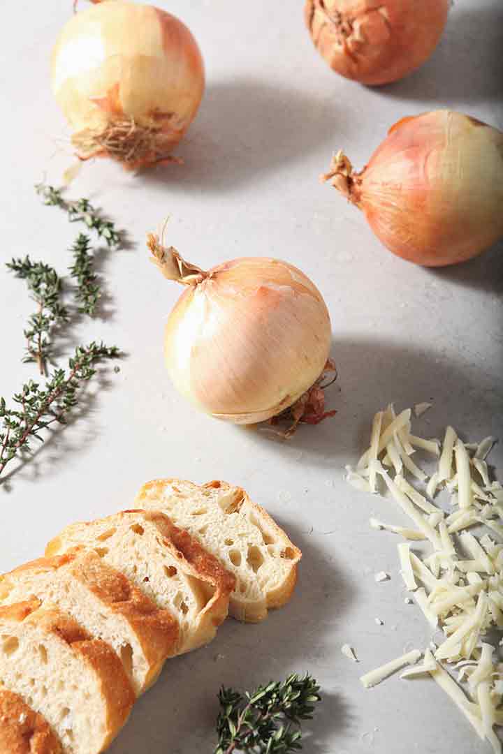 Ingredients for Instant Pot French Onion Soup--onions, bread, cheese, thyme--are laid out on a light-colored background