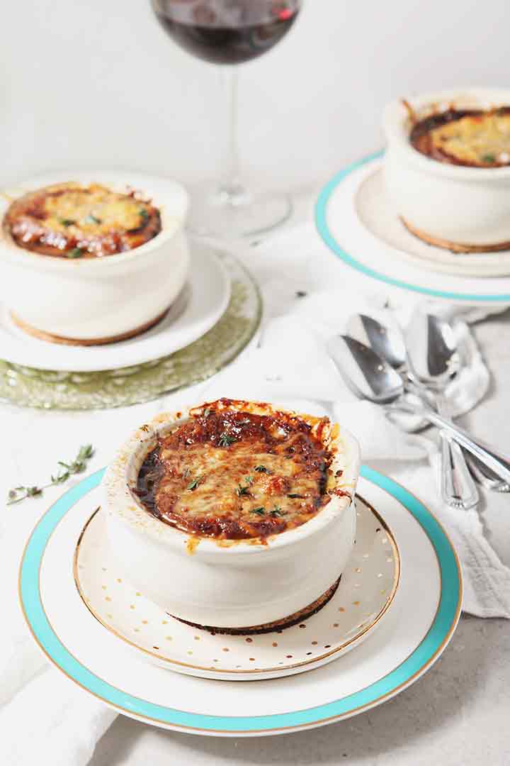 Three crocks holding Instant Pot French Onion Soup are served with red wine