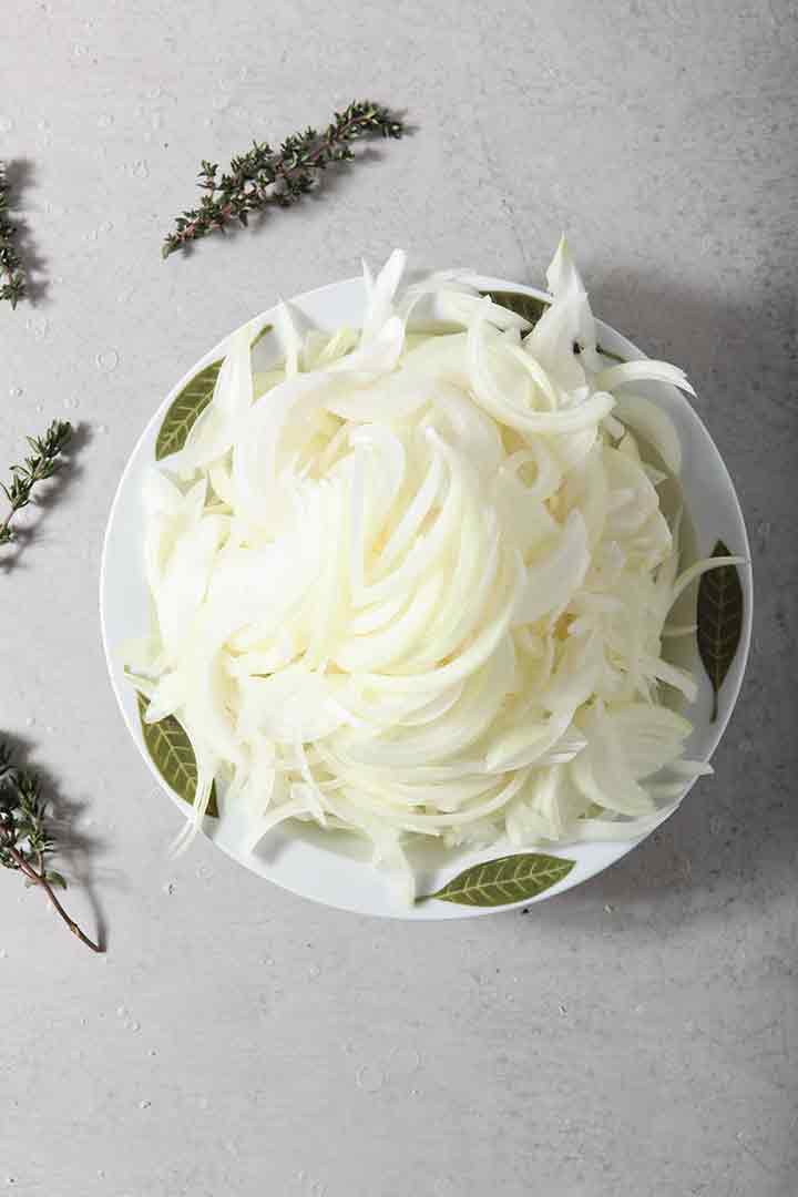 Slivered onions in a bowl, surrounded by fresh thyme