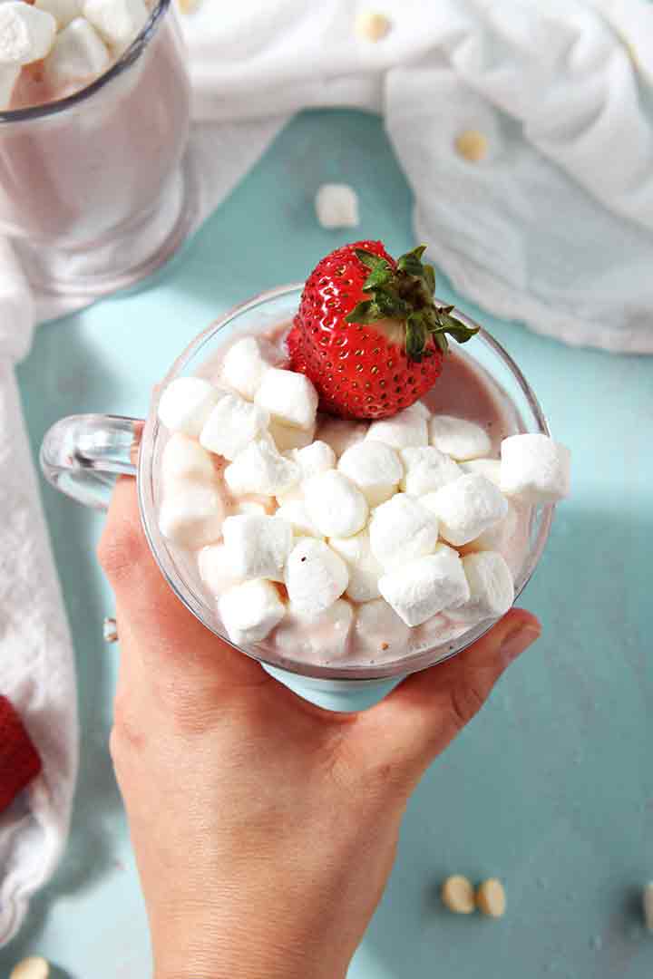 A woman holds a mug of Strawberry White Hot Chocolate in her hand