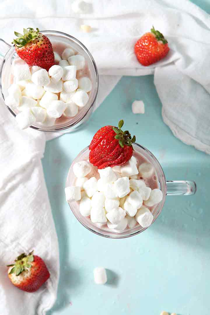 Two Strawberry White Hot Chocolates in mugs, garnished with marshmallows and strawberries, from above