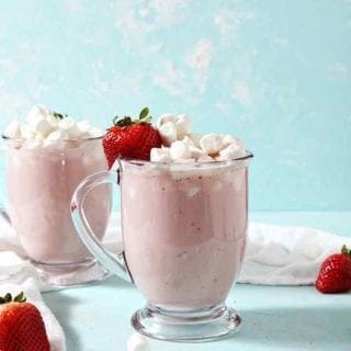 Two mugs of Strawberry White Hot Chocolate are garnished with marshmallows and strawberries