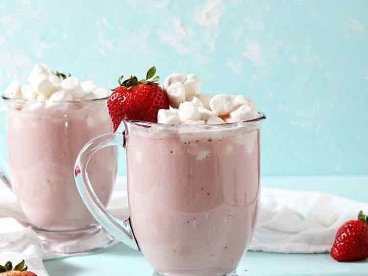 Two mugs of Strawberry White Hot Chocolate are garnished with marshmallows and strawberries