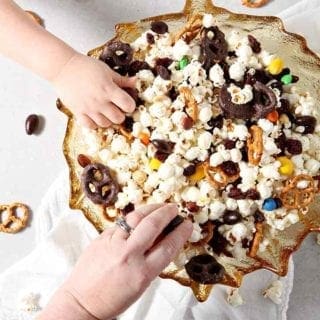 Two people reach into a bowl of Sweet-and-Salty Popcorn Mix