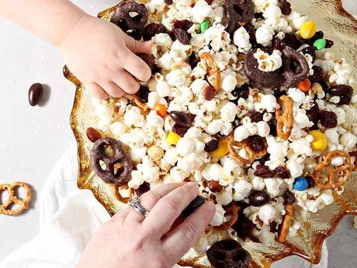 Two people reach into a bowl of Sweet-and-Salty Popcorn Mix