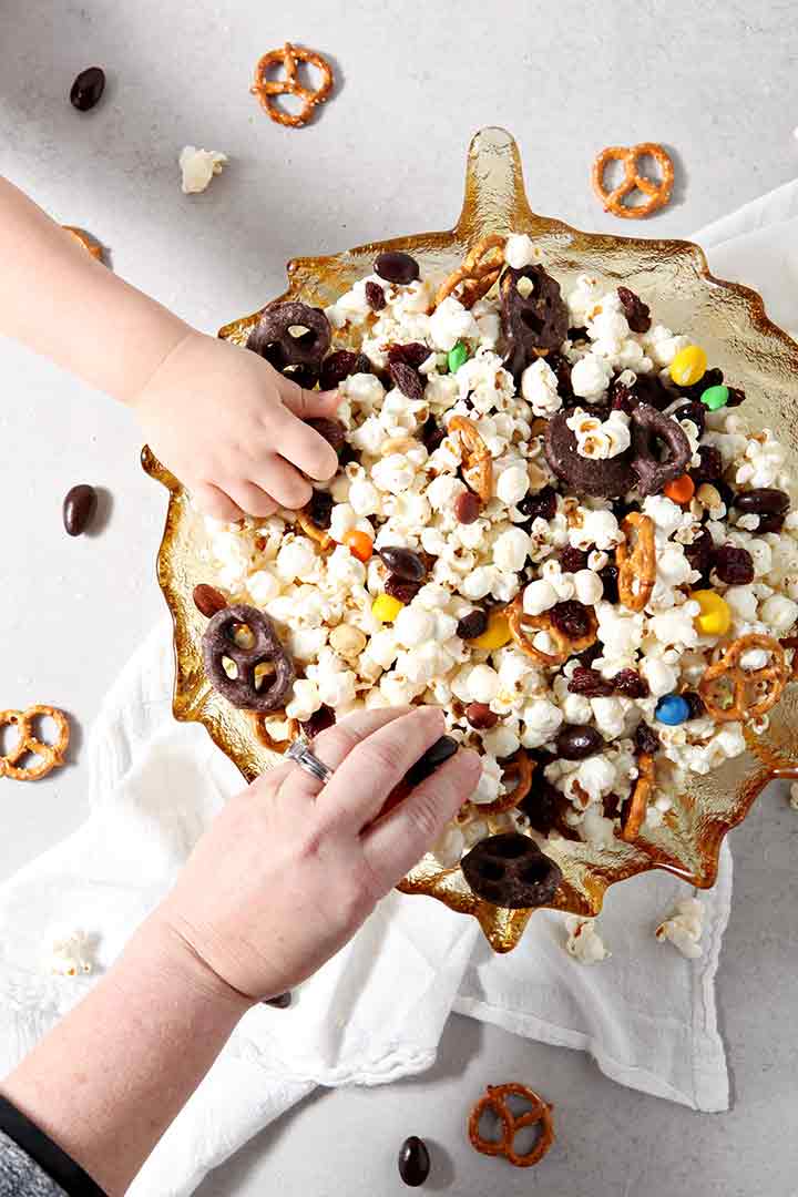 Two people reach into a bowl of Sweet-and-Salty Popcorn Mix