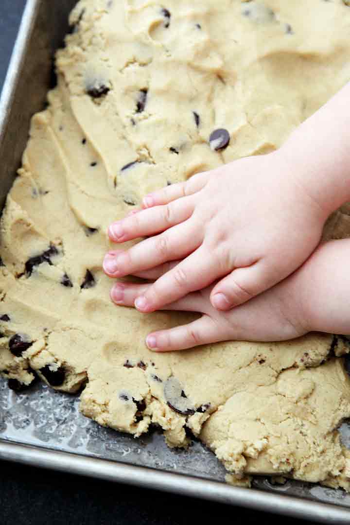 A girl presses cookie bar batter into a baking dish before baking