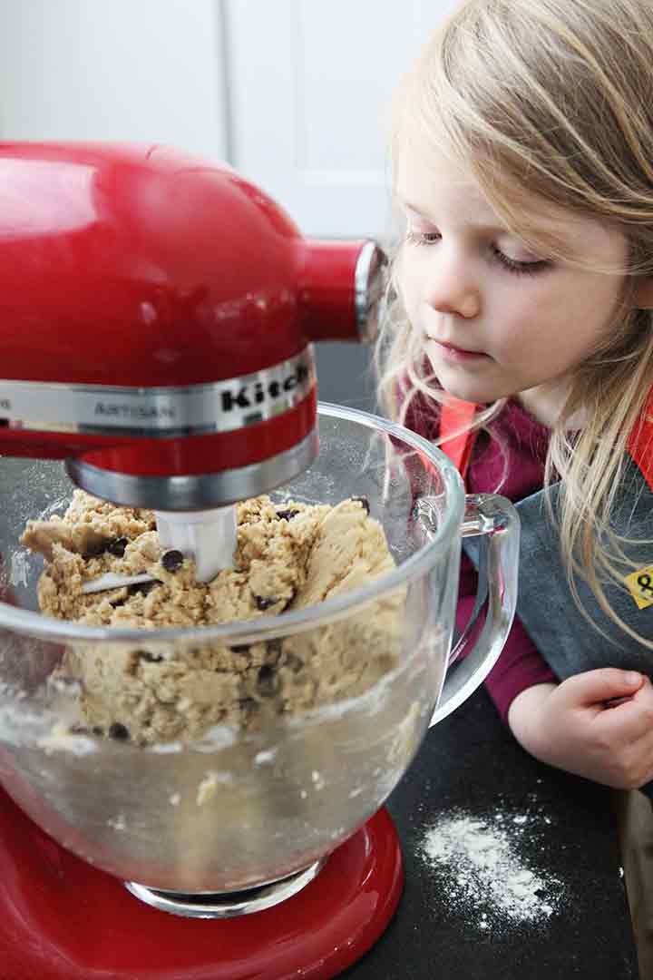 A girl watches Chocolate Chip Cookie Bar batter mix in a stand mixer