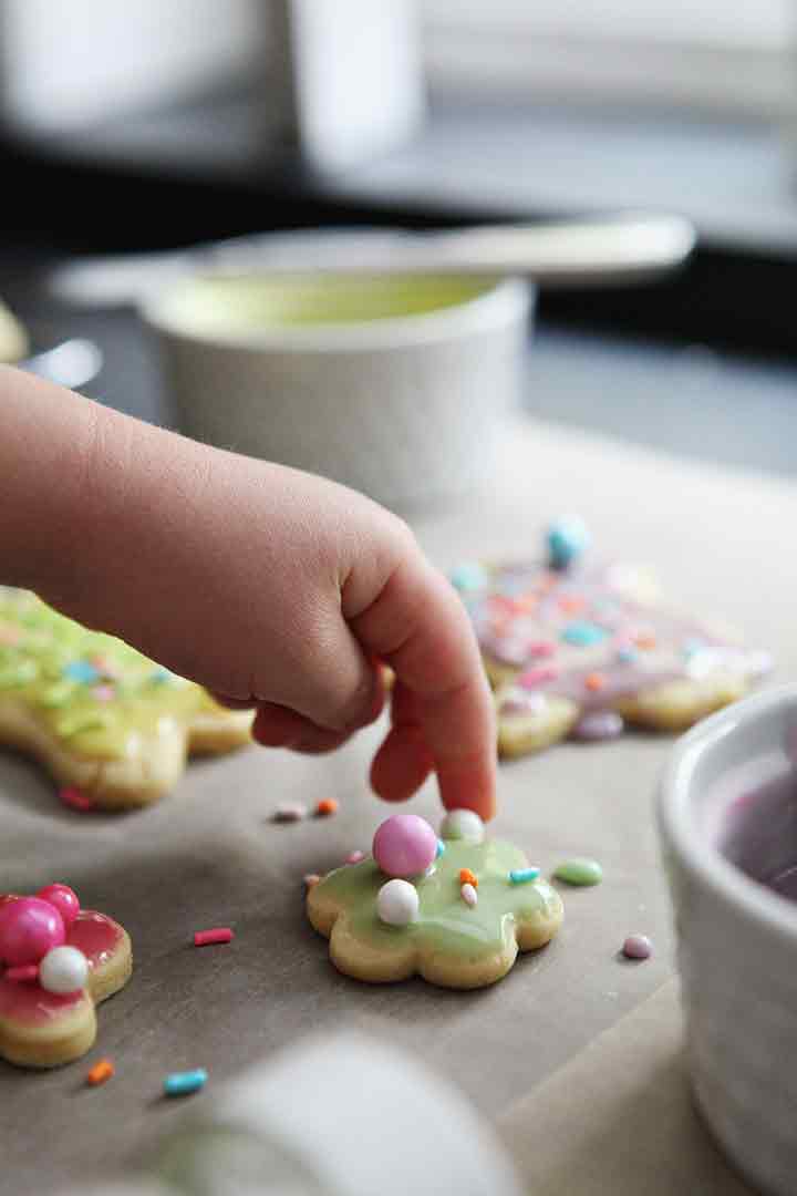 A girl places decorative sprinkles onto lemon sugar cookies