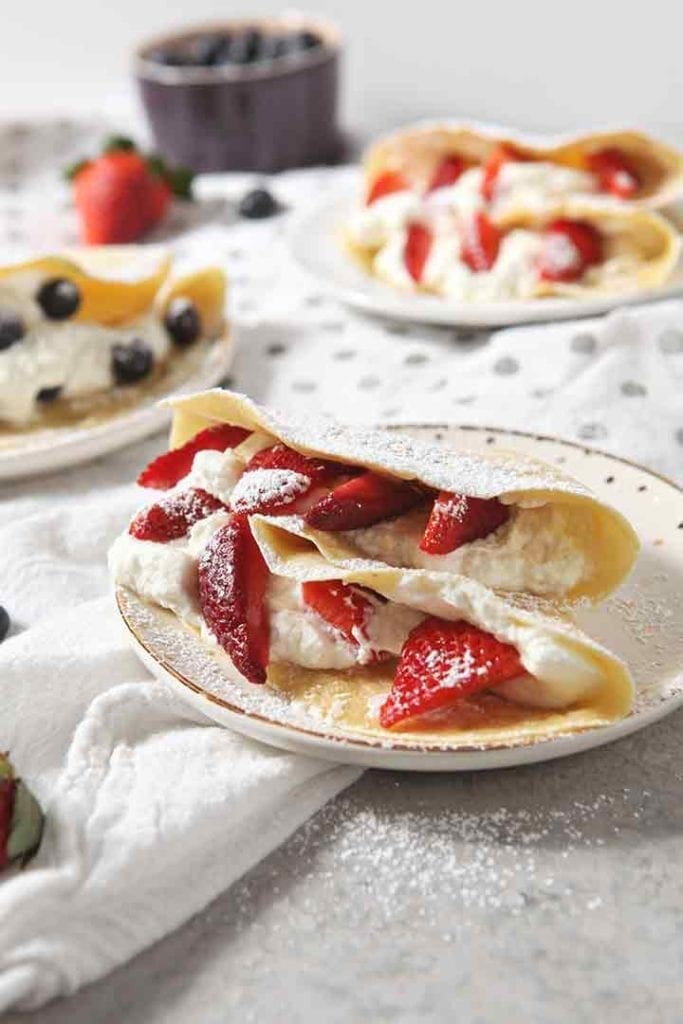 A breakfast crepe stuffed with whipped cream and strawberries on a white towel