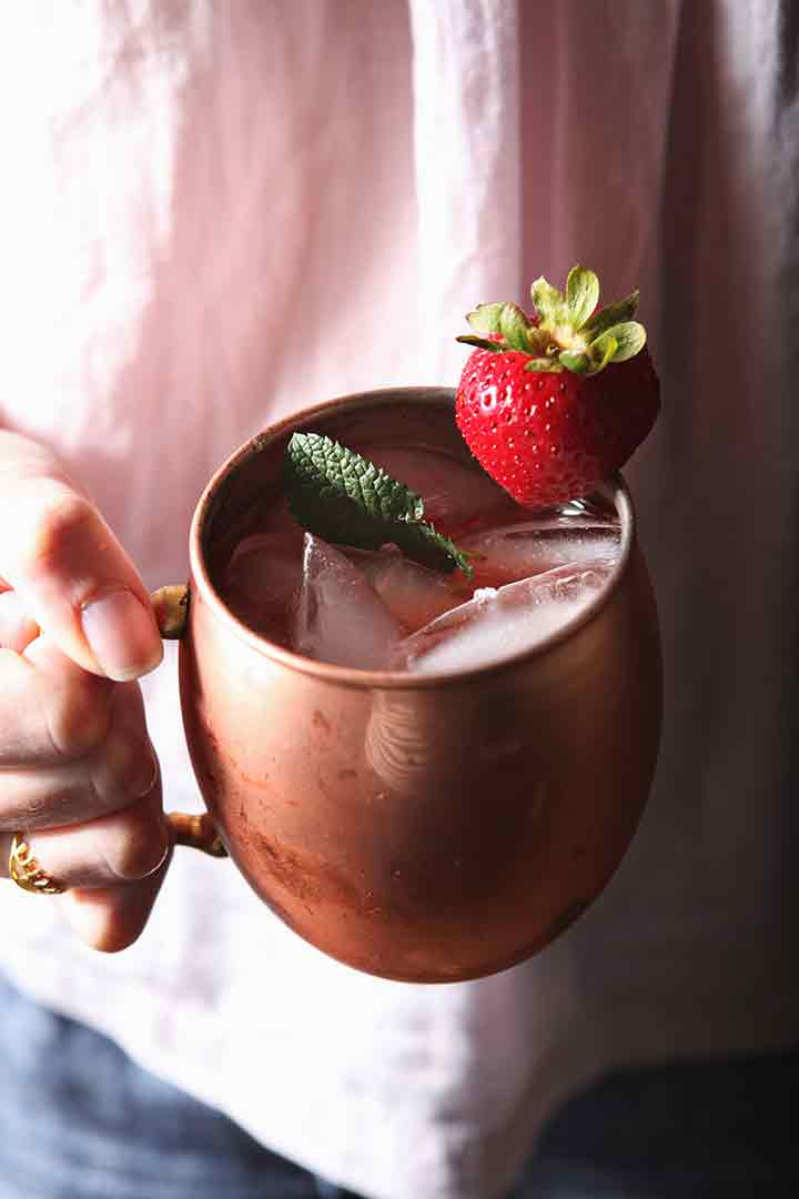 A woman holds a copper mug holding a Strawberry Mule