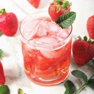 A glass holds a mixed Strawberry Moscow Mule, surrounded by strawberries and mint