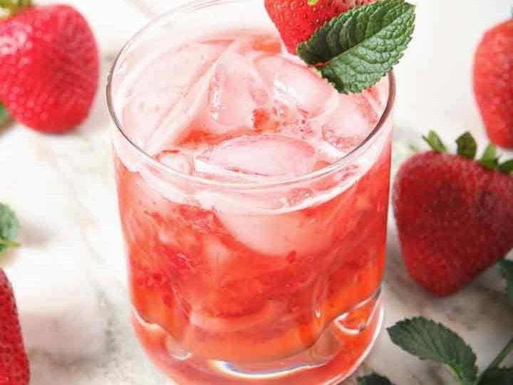 A glass holds a mixed Strawberry Moscow Mule, surrounded by strawberries and mint