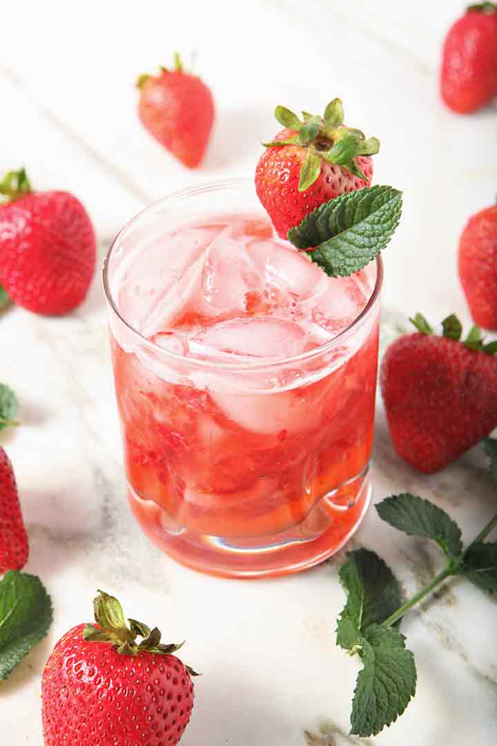 A glass holds a mixed Strawberry Moscow Mule, surrounded by strawberries and mint