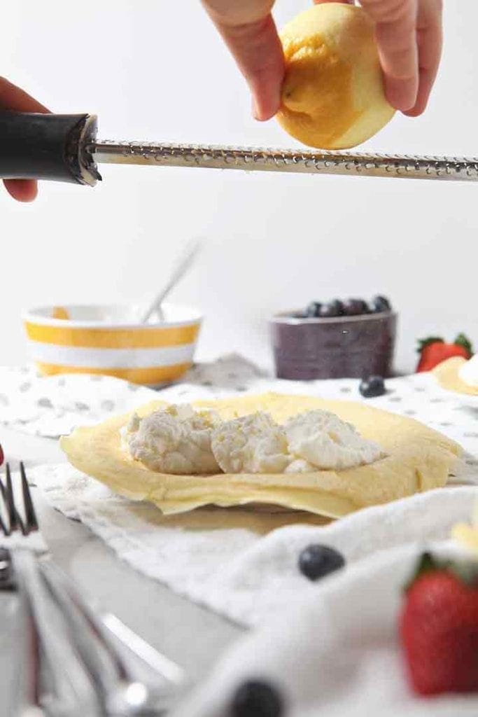 A lemon is zested on top of a sweet crepe and its whipped cream filling before fruit is added