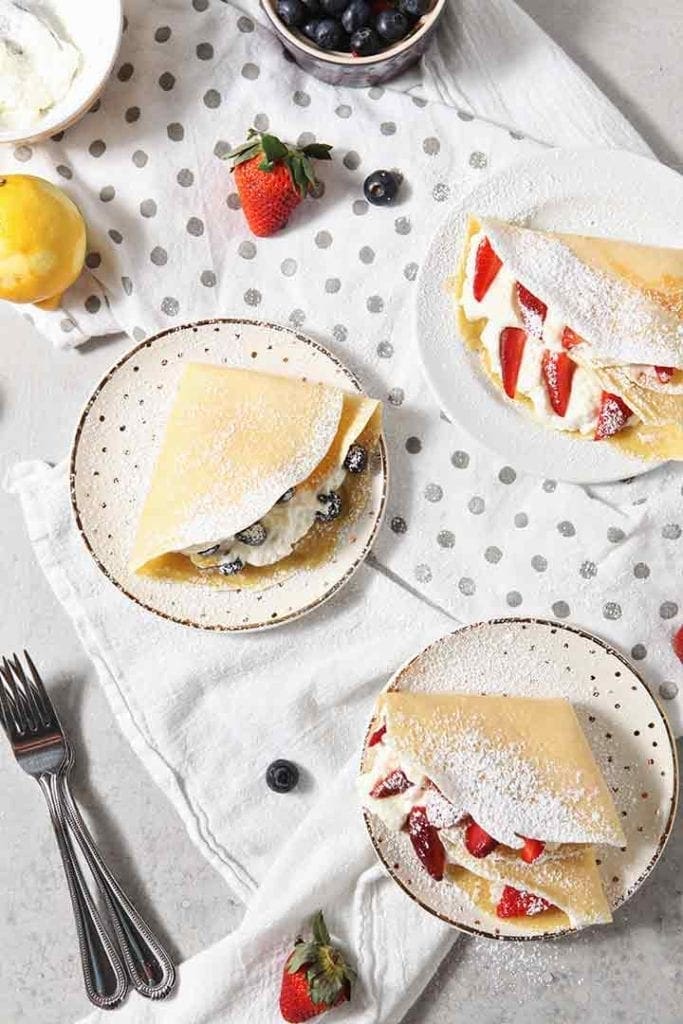 Three Sweet Breakfast Crepes are surrounded by fruit and served warm