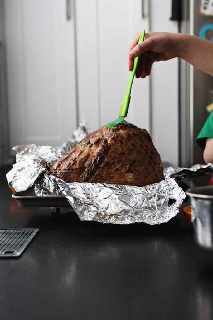 A woman brushes bourbon orange glaze onto a spiral ham before baking