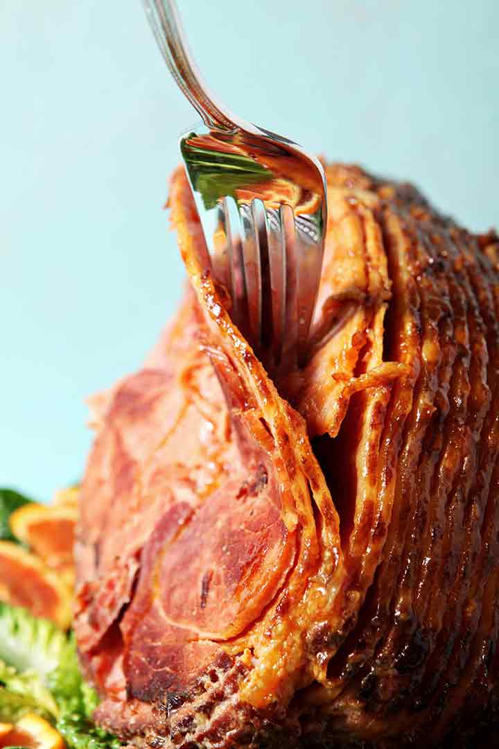 A serving fork pulls apart pieces of a Baked Ham with Bourbon Orange Glaze