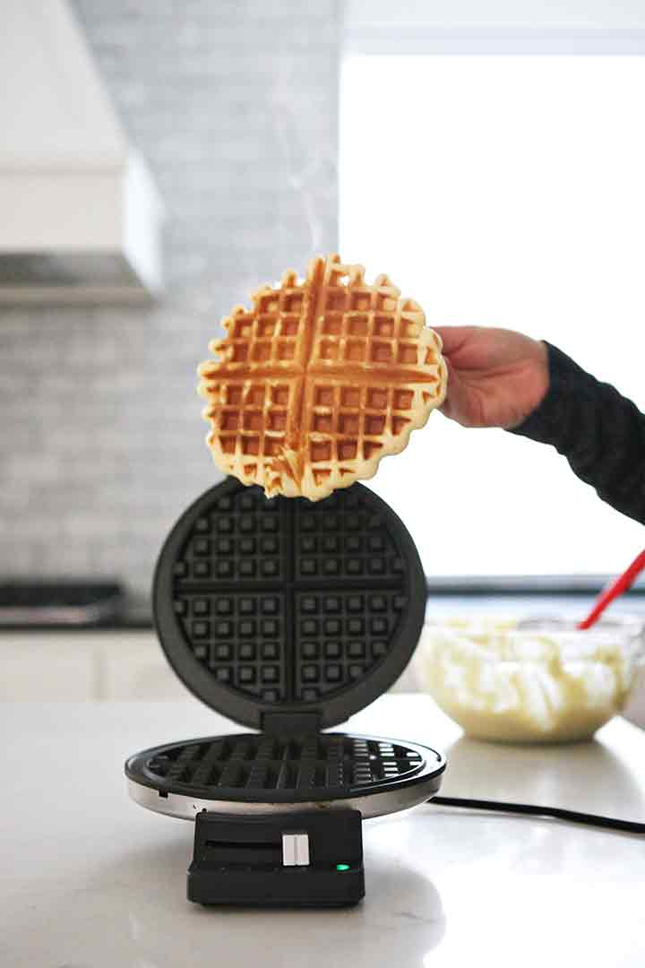 A woman pulls a hot waffle off the waffle iron