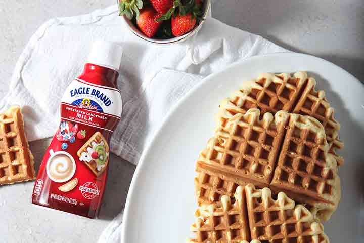 A bottle of Eagle Brand sweetened condensed milk lies next to a platter of waffles