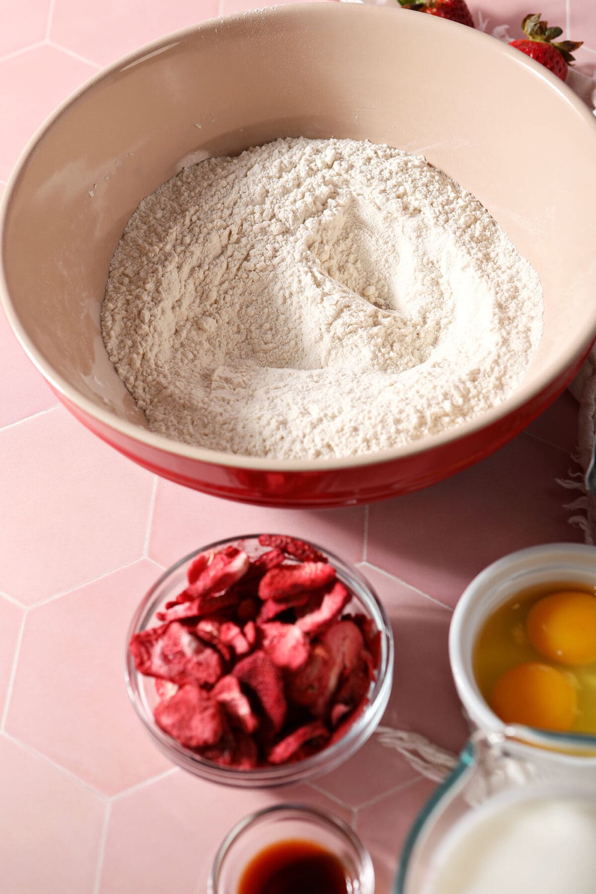 Ingredients to make waffles in bowls on a pink tiled surface