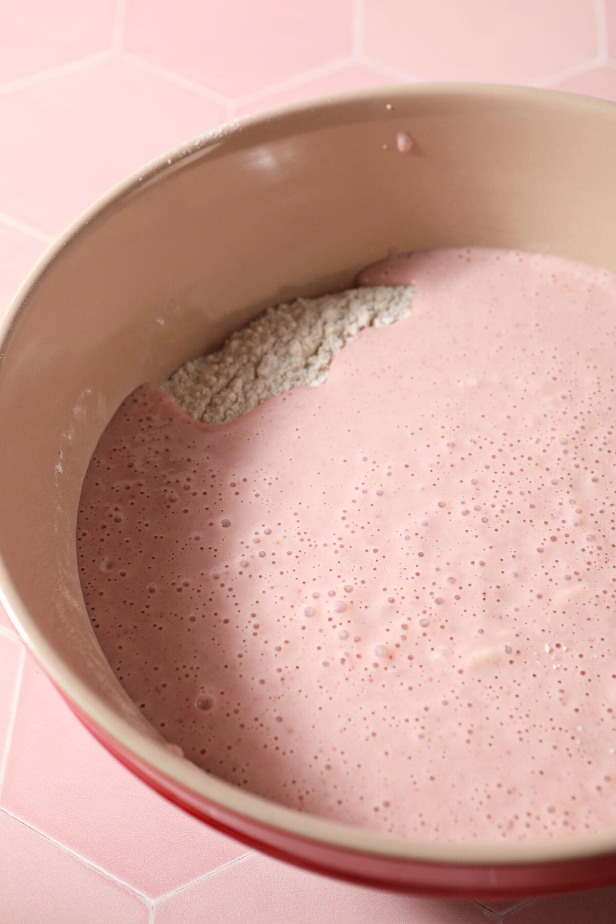 Wet ingredients sit on top of dry ingredients for waffles in a mixing bowl on a pink surface