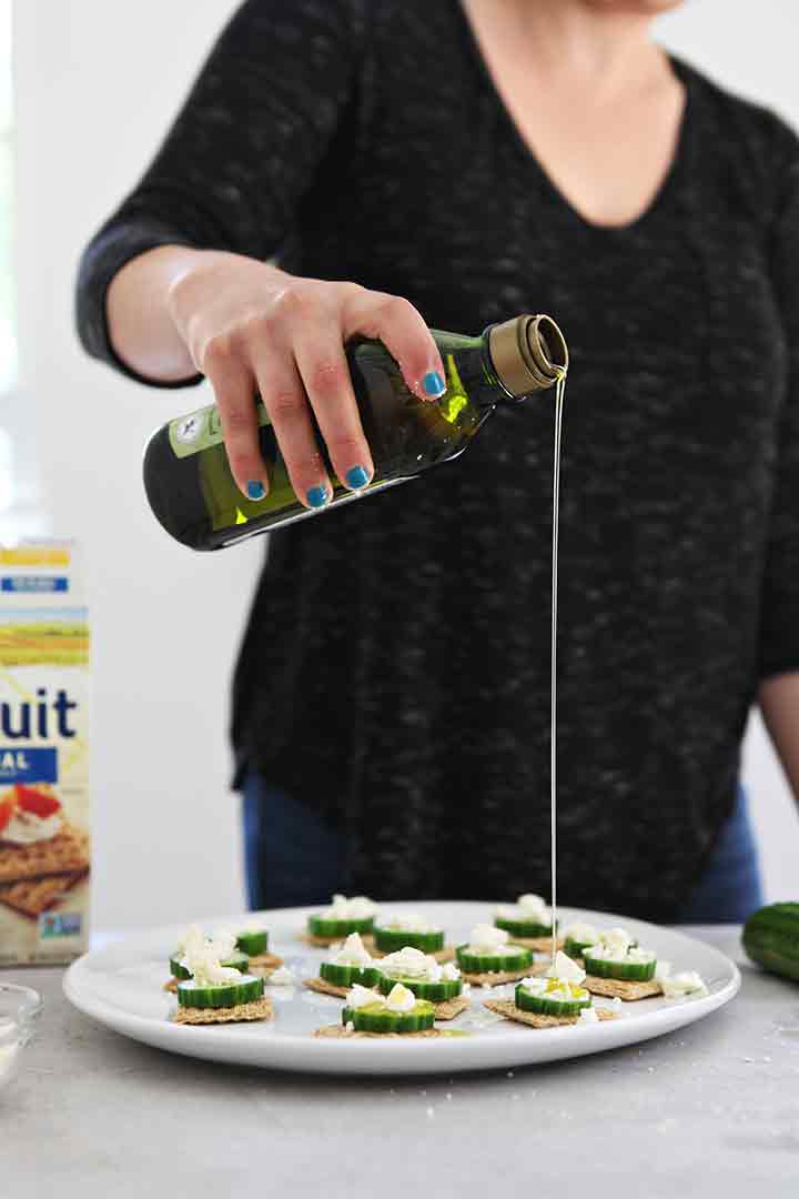 A woman drizzles olive oil on top of the cucumber appetizer