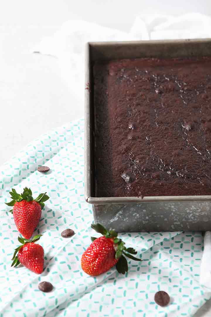 A chocolate sheet cake is shown on a light-colored background after coming out of the oven