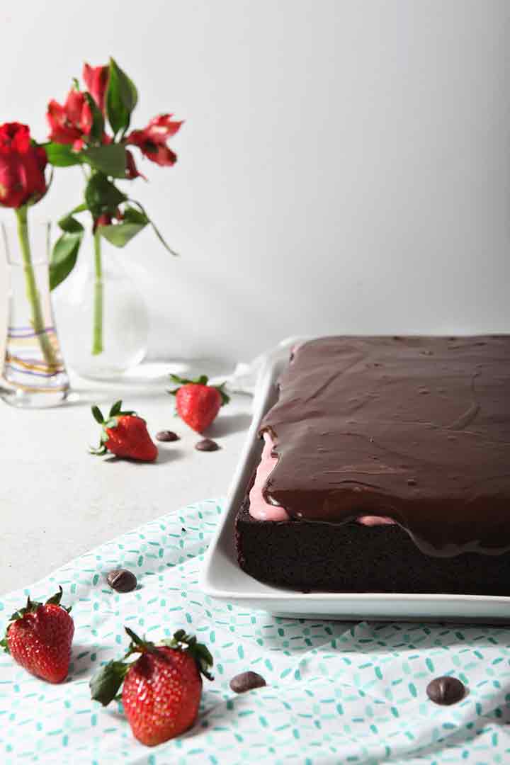 A chocolate sheet cake, drizzled with strawberry cream cheese frosting and chocolate ganache, is served on a light-colored background