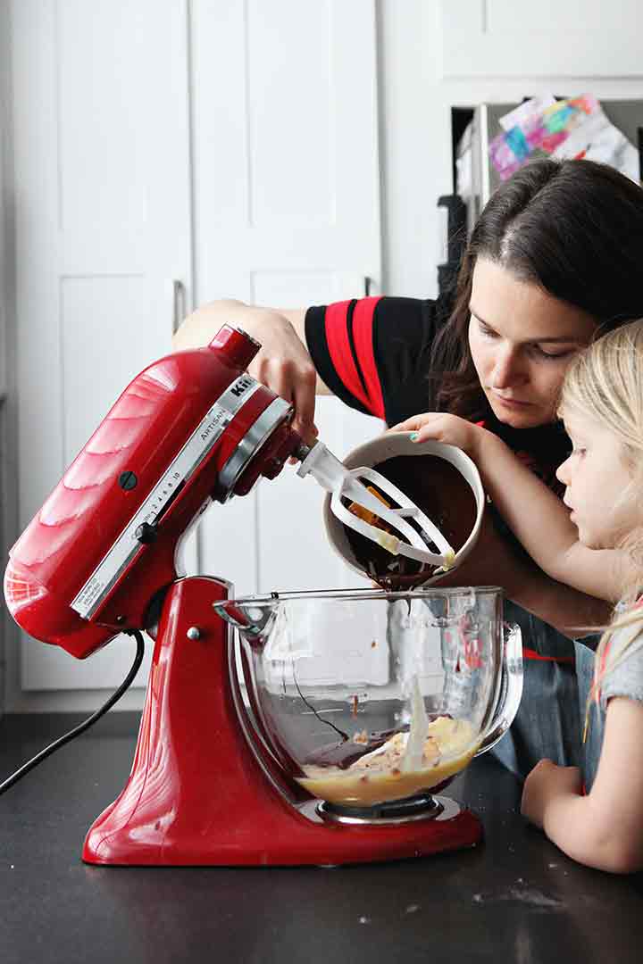 A woman and a girl pour melted chocolate into the bowl of a stand mixer