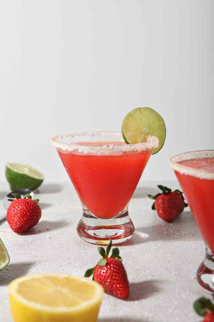 Close up of two Strawberry Margaritas, surrounded by fresh fruit