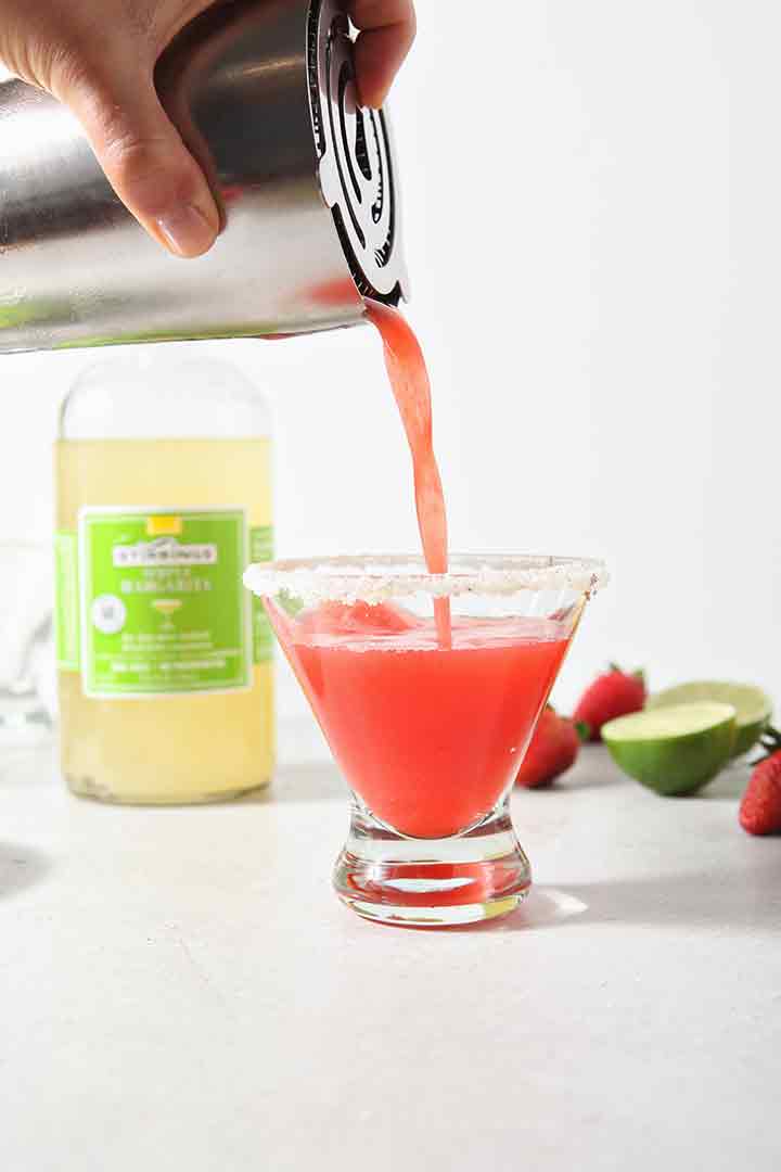 A pink drink pours into a prepared glass