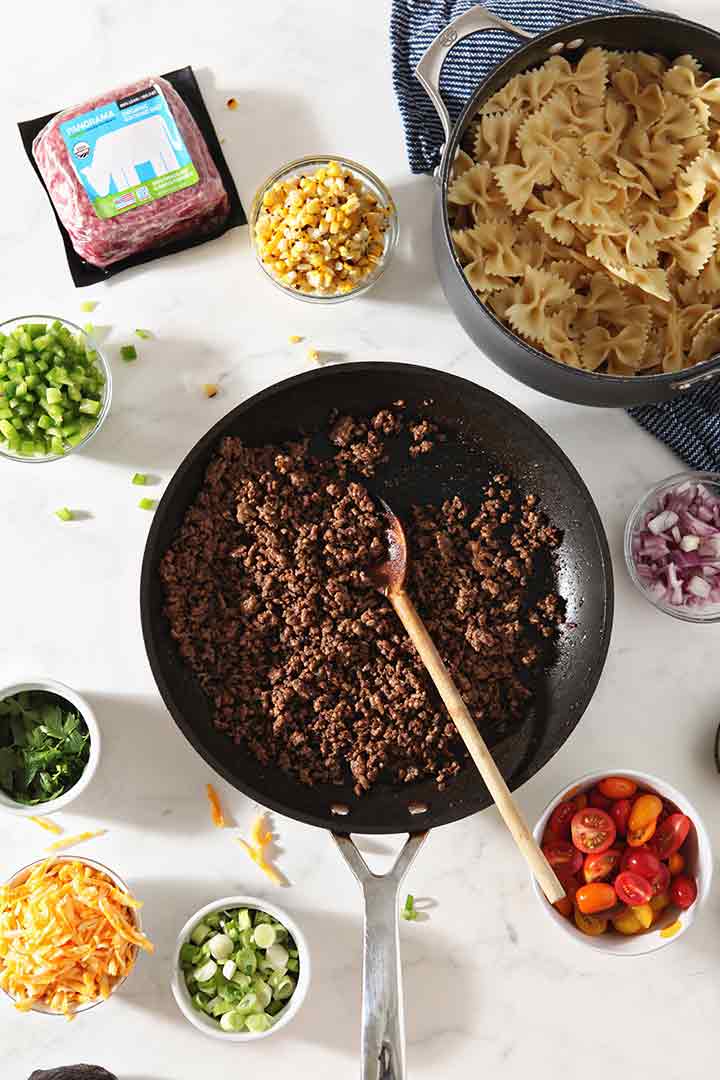 Cooked ground beef is shown in a skillet, after cooking, surrounded by other ingredients