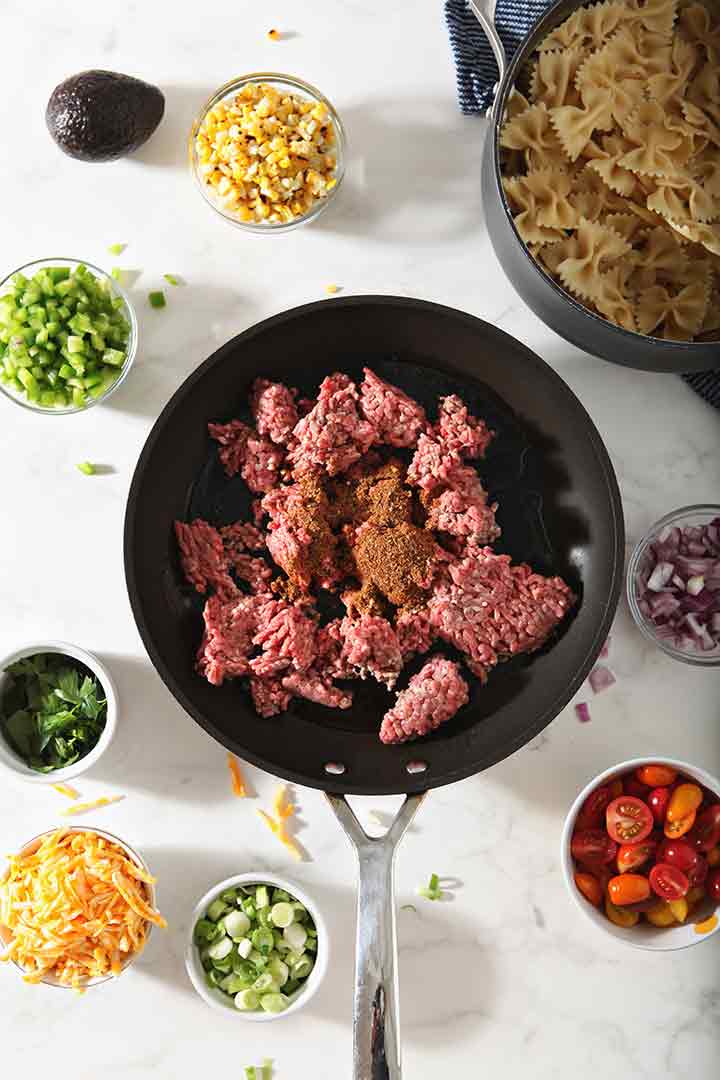 Ground beef is shown in a skillet, surrounded by other ingredients