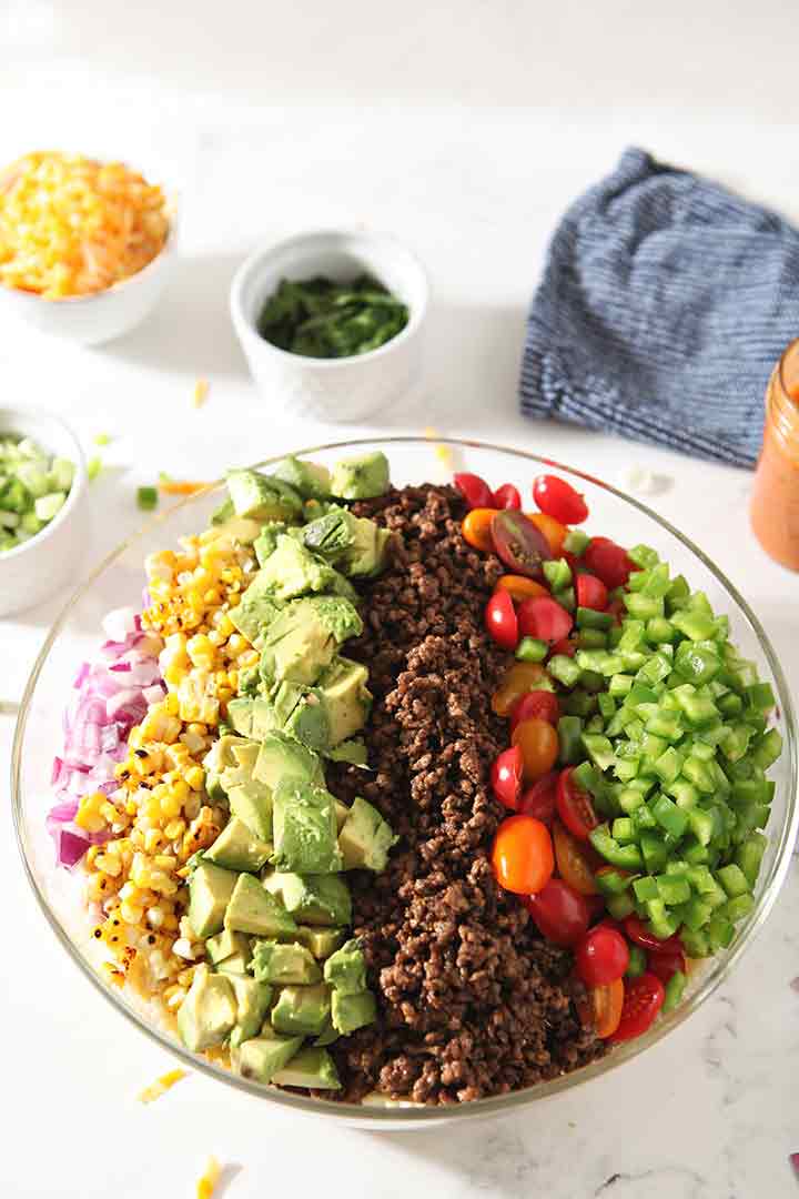 Ingredients for Taco Pasta Salad are shown lined up on top of the pasta, before tossing