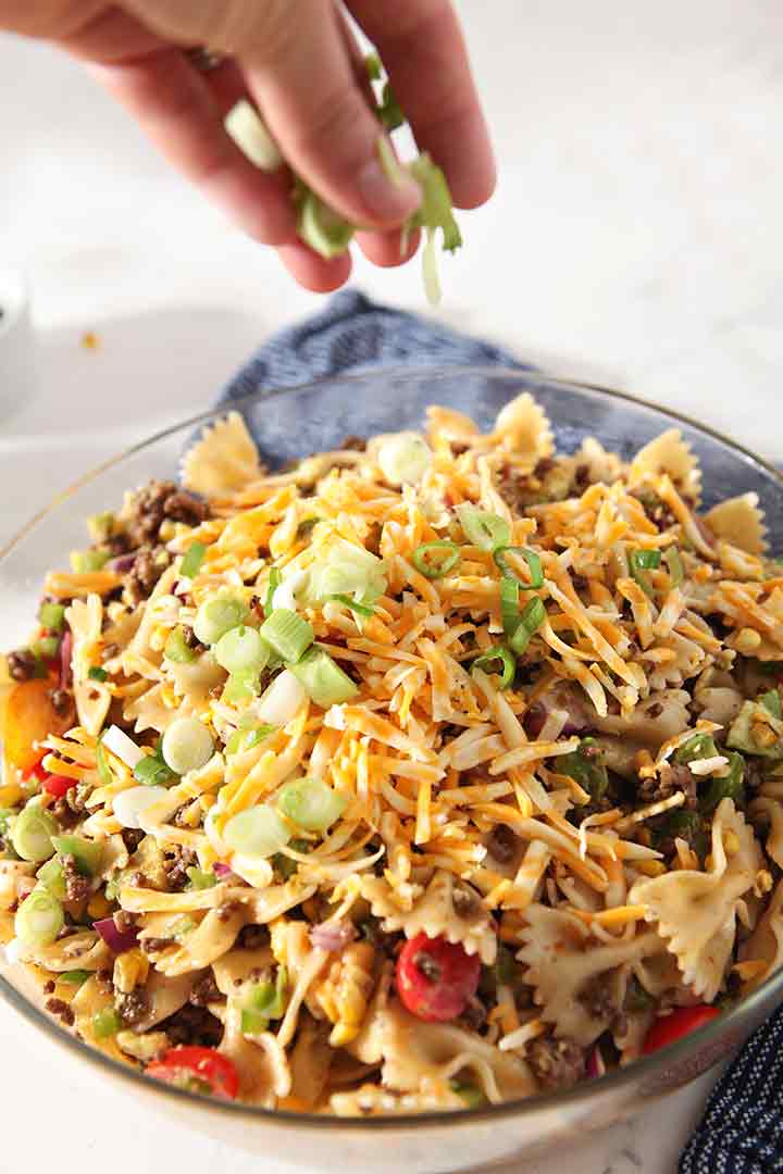 A woman sprinkles green onions on top of a salad